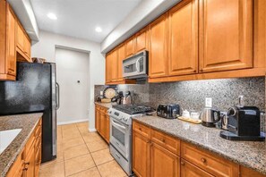 A kitchen with wooden cabinets, a stainless steel refrigerator, a microwave, a stove, and various appliances on the countertop.