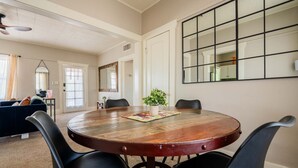 Una mesa redonda de madera con cuatro sillas, un espejo en la pared y una puerta que da a otra habitación.