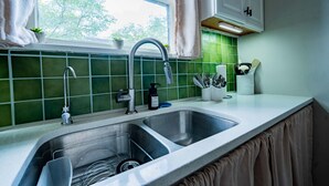 Una cocina con un lavamanos doble, azulejos verdes, un ventanal con cortinas y un armario sobre el lavamanos.