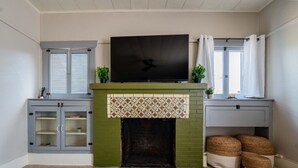 Una sala de estar con chimenea, televisor encima y ventana con cortinas.