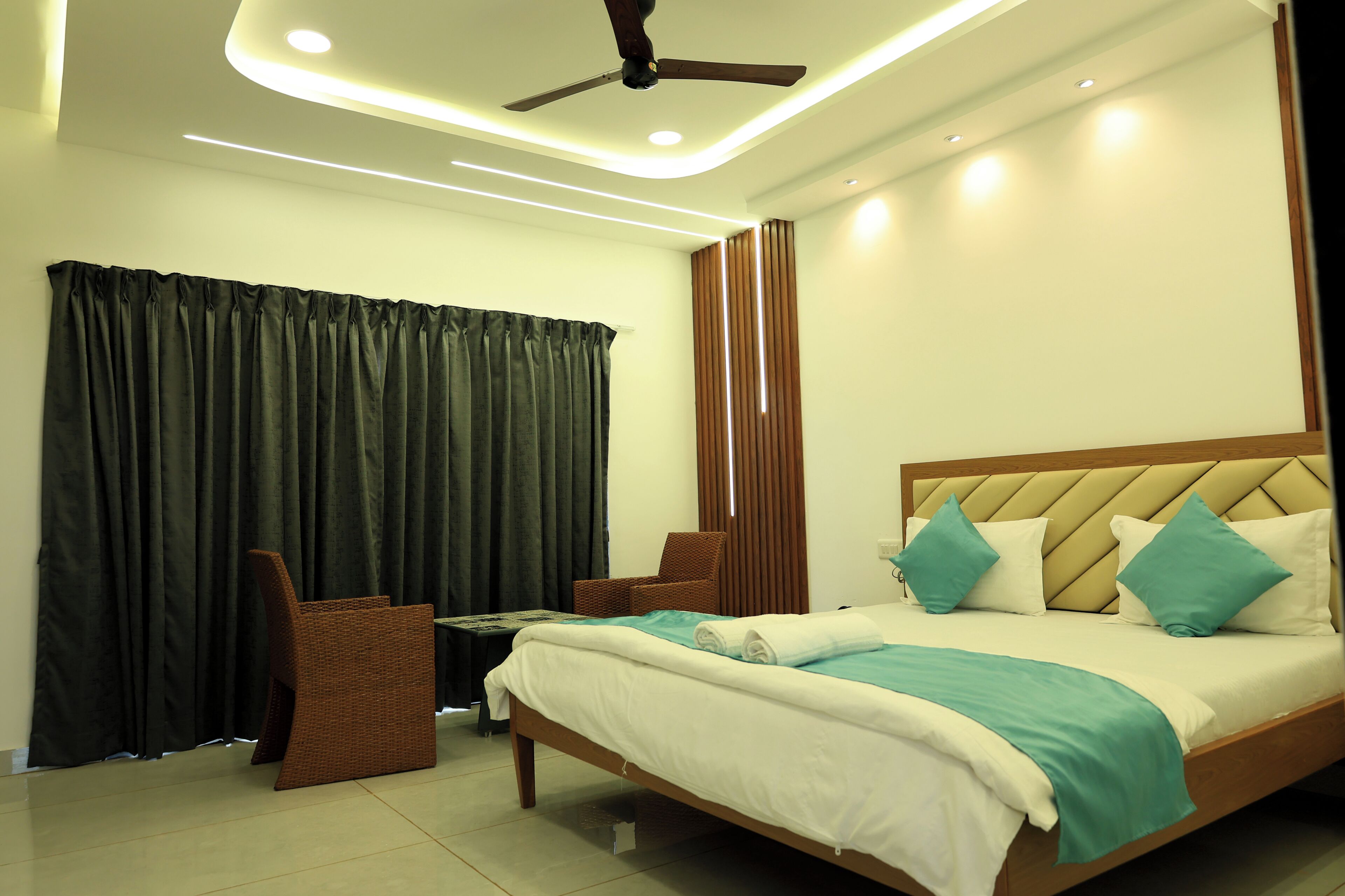 A hotel room with a bed, a chair, a small table, and a ceiling fan.