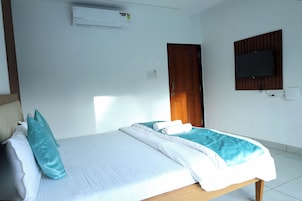 Habitación de hotel con cama, televisor montado en la pared y aire acondicionado sobre la cama.