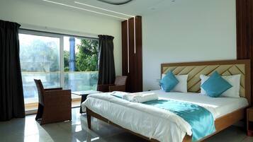 Habitación de hotel con una cama grande, vistas a zonas verdes y un balcón con mesa y sillas.