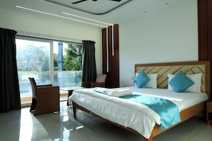 A hotel room with a large bed, a view of greenery outside, and a balcony with a table and chairs. - Prasanna Beach Resort - 150 meters to Kihim Beach (Alibag)