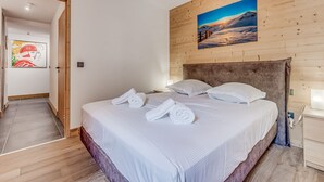 A bedroom with a wooden headboard, a painting of a mountain landscape, and neatly folded towels on the bed. - Family apartment 8 pers, balcony, parking, wifi included (Champagny-en-Vanoise)