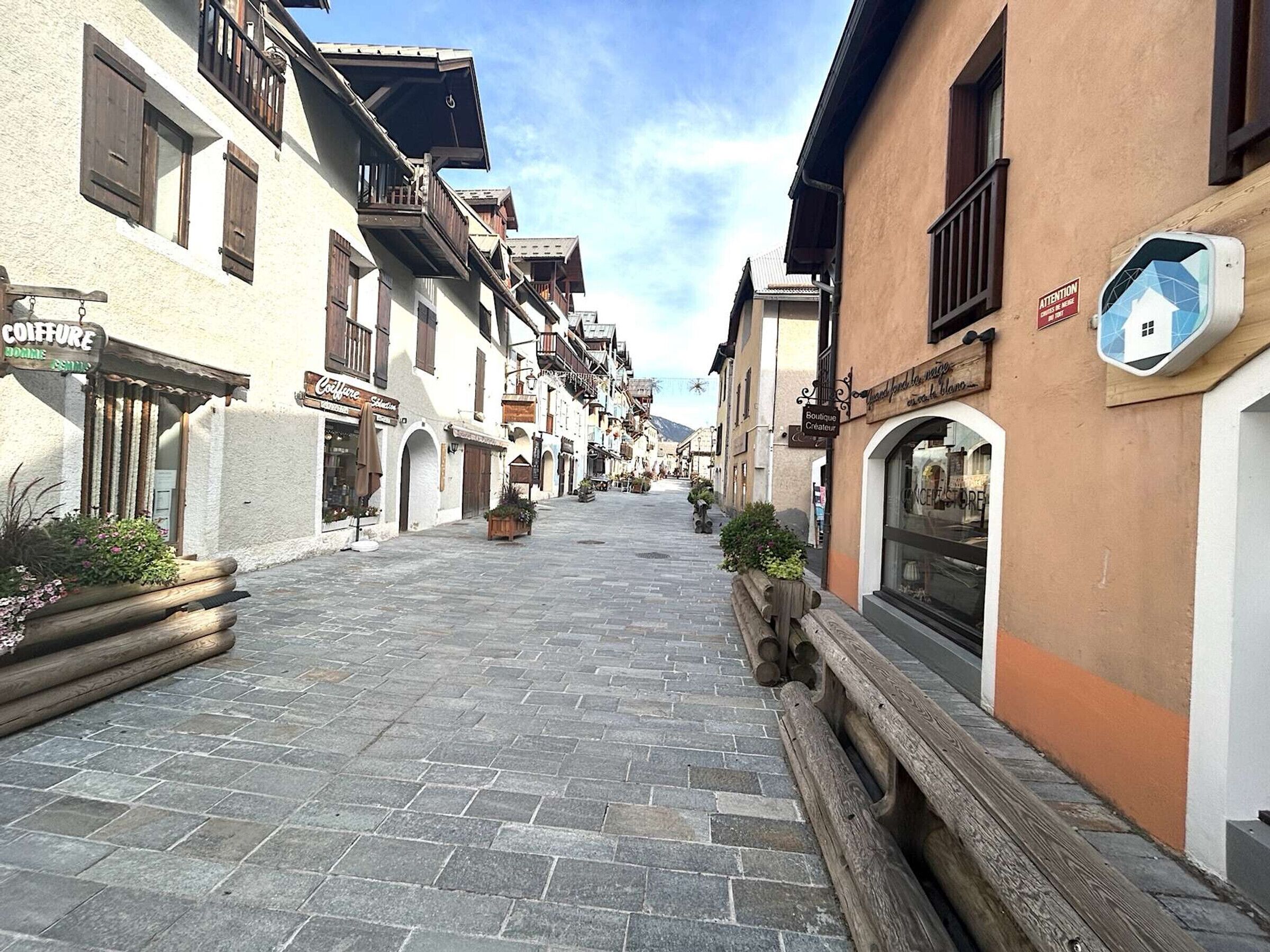 A cobblestone street lined with traditional buildings, some with balconies and signage for local businesses.