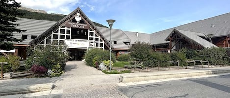 Un edificio comercial con una destacada torre de reloj, un cartel del Office de Tourism y un acceso pavimentado rodeado de vegetación.