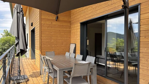 Eine Holzterrasse mit Tisch und Stühlen, einer Glastür und einem überdachten Außenbereich.