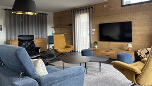 Ein modernes Wohnzimmer mit großem Flachbildfernseher, einer Couch, einem Sessel und einem Couchtisch.