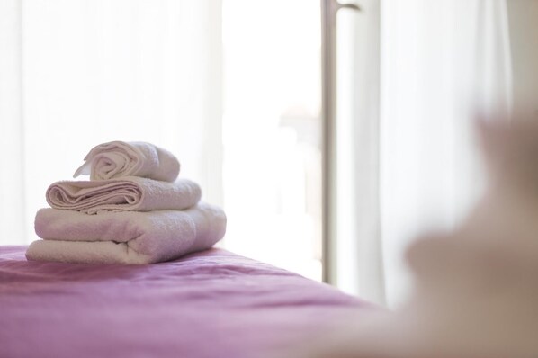 A stack of folded towels on a bed with a purple bedspread.