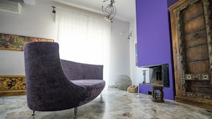 Une pièce avec un fauteuil violet, une cheminée, une porte décorative et un sol en marbre.