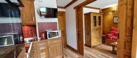 A compact kitchen with wooden cabinets, a microwave, and a TV above the counter.