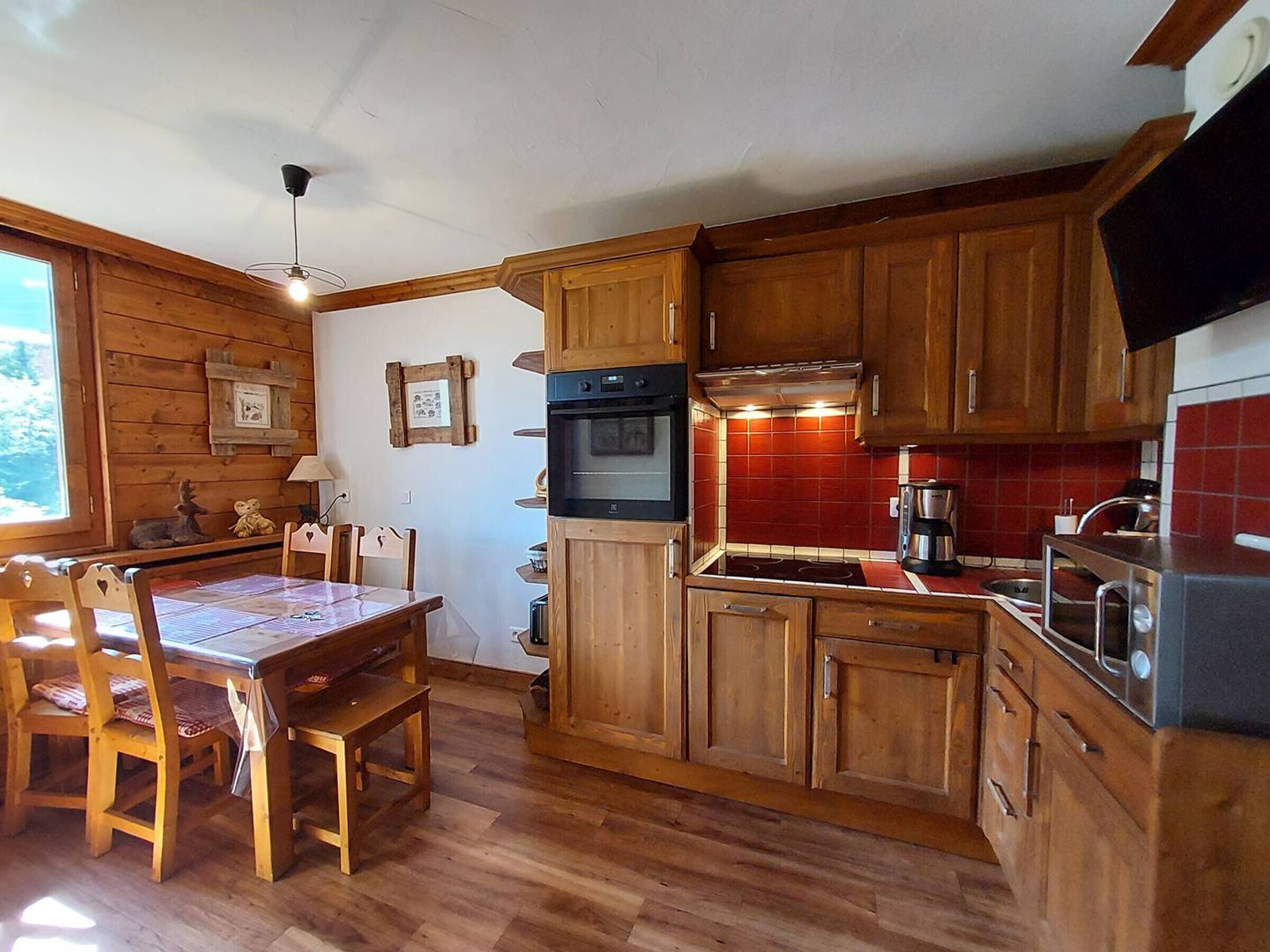 Et hyggeligt køkken med træskabe, et spisebord med stole og en backsplash i røde fliser.