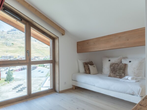 A bedroom with a large window, wooden beams, and a white bed with multiple pillows.