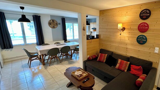 Ein modernes Wohnzimmer mit einer Couch, einem Esstisch mit Stühlen, einer Holzwand mit Dekorationplatten und einer Tür mit Schlüsselloch.