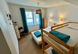 Un dormitorio con cama de madera, una mesita de noche, una silla, un radiador, una ventana con cortinas y una lámpara fijada a la pared.