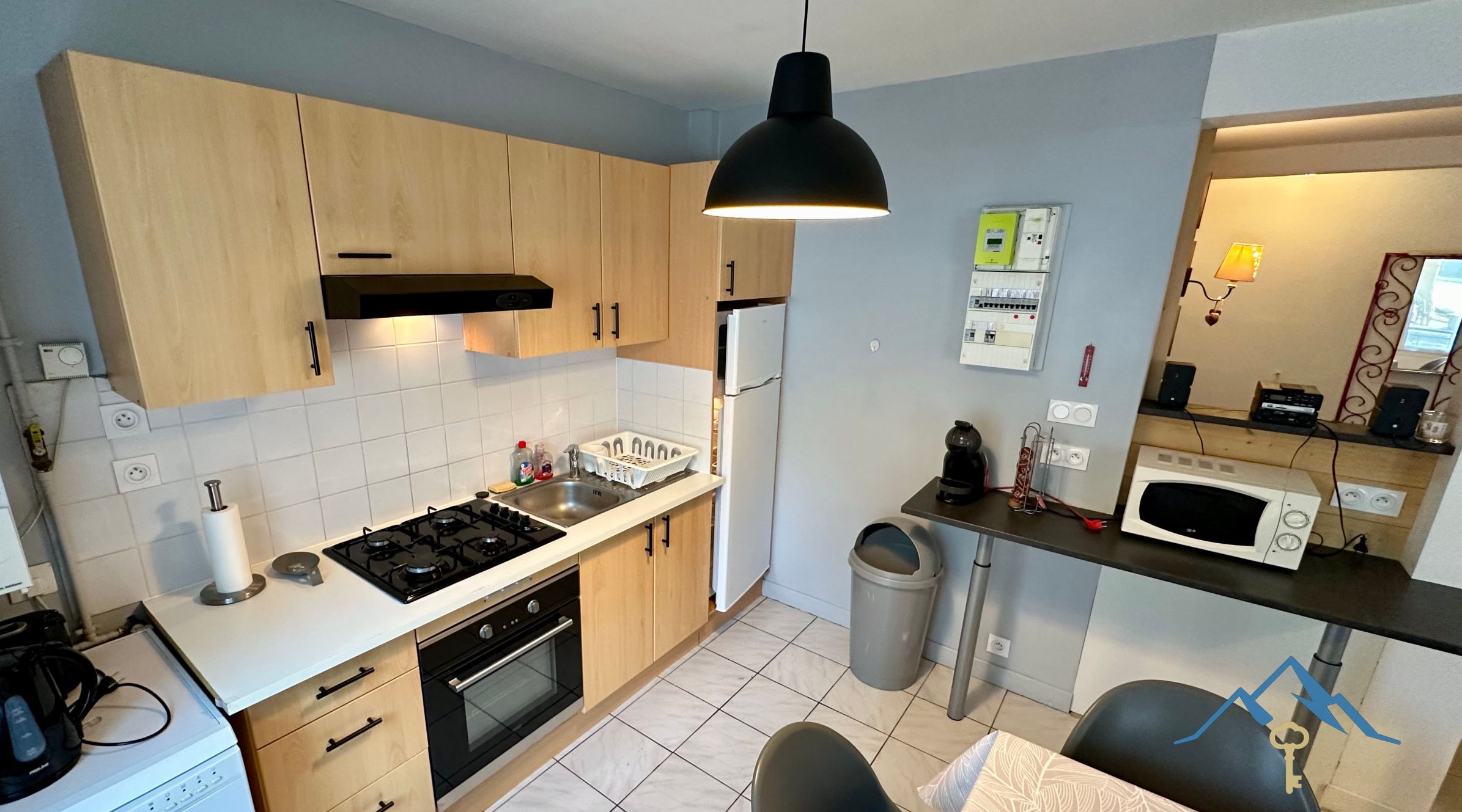 Une cuisine de taille réduite, dotée de meubles en bois, d’une cuisinière à gaz, d’un four à micro-ondes et d’un évier.