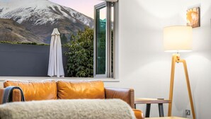 Une pièce comprenant un canapé en cuir, une table, un lampadaire, une fenêtre donnant sur la montagne et une plante.