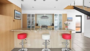 Une cuisine moderne dotée d’un îlot central, de trois tabourets de bar et d’un escalier menant à un niveau supérieur.