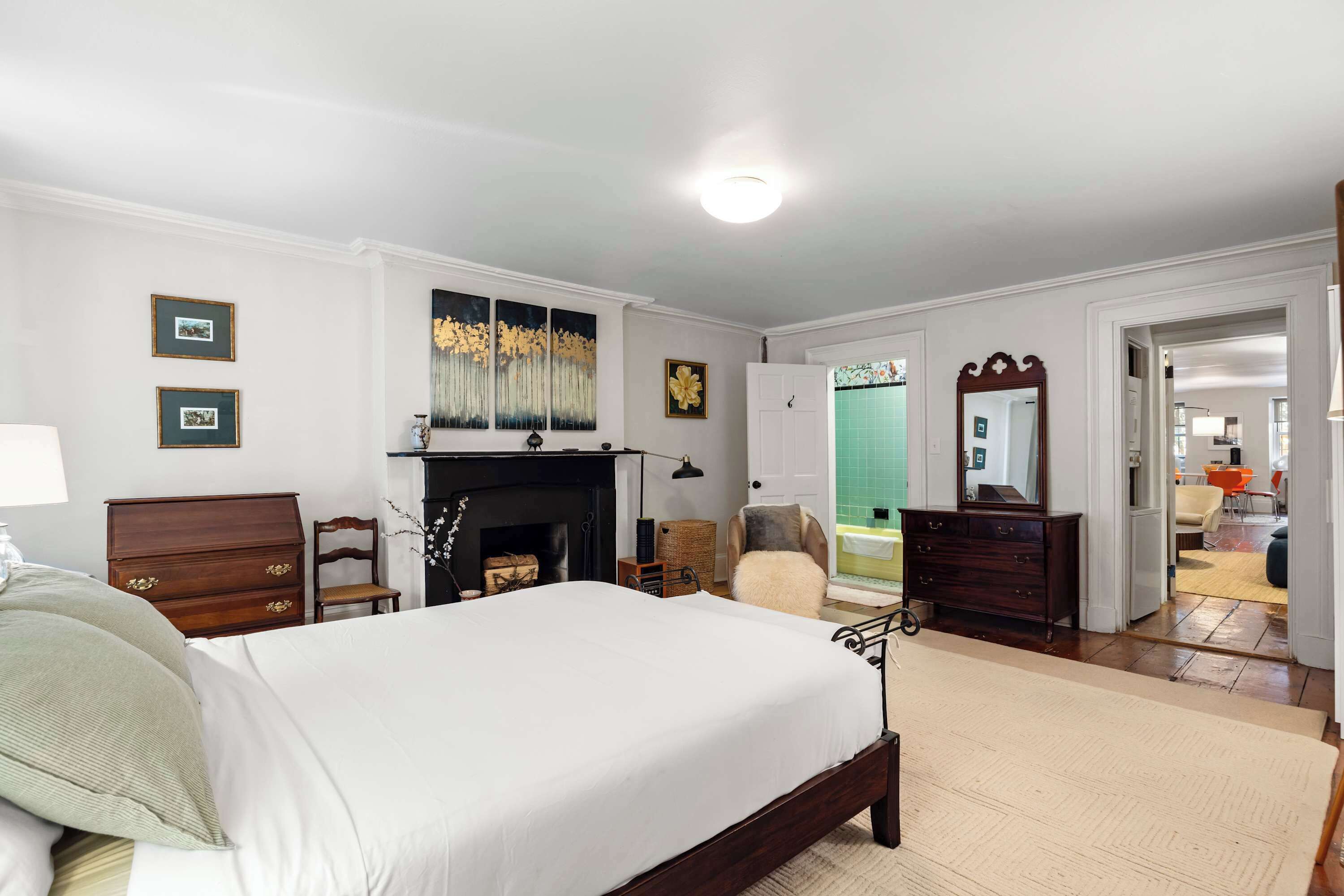 A bedroom with a large bed, a fireplace, a mirror, and a door leading to another room.