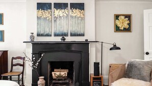 Un salon avec une cheminée noire, un vase orné de branches, un fauteuil, un canapé et une lampe.