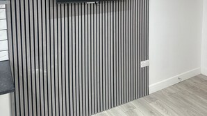 Habitación con televisor de pantalla plana en una pared a rayas, un enchufe y suelo de madera.