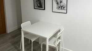 Una mesa de comedor blanca con dos sillas, una puerta de madera y tres cuadros en la pared.