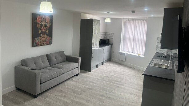 Una sala moderna con un sofá gris, una cocina con encimera negra y un comedor con mesa y sillas negras.