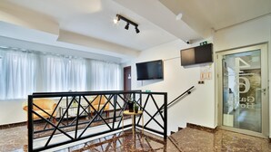 A hotel lobby with a marble floor, a sofa, a TV mounted on the wall, and a glass door with a reflection. - Garni House 46 Plus (Belgrade)