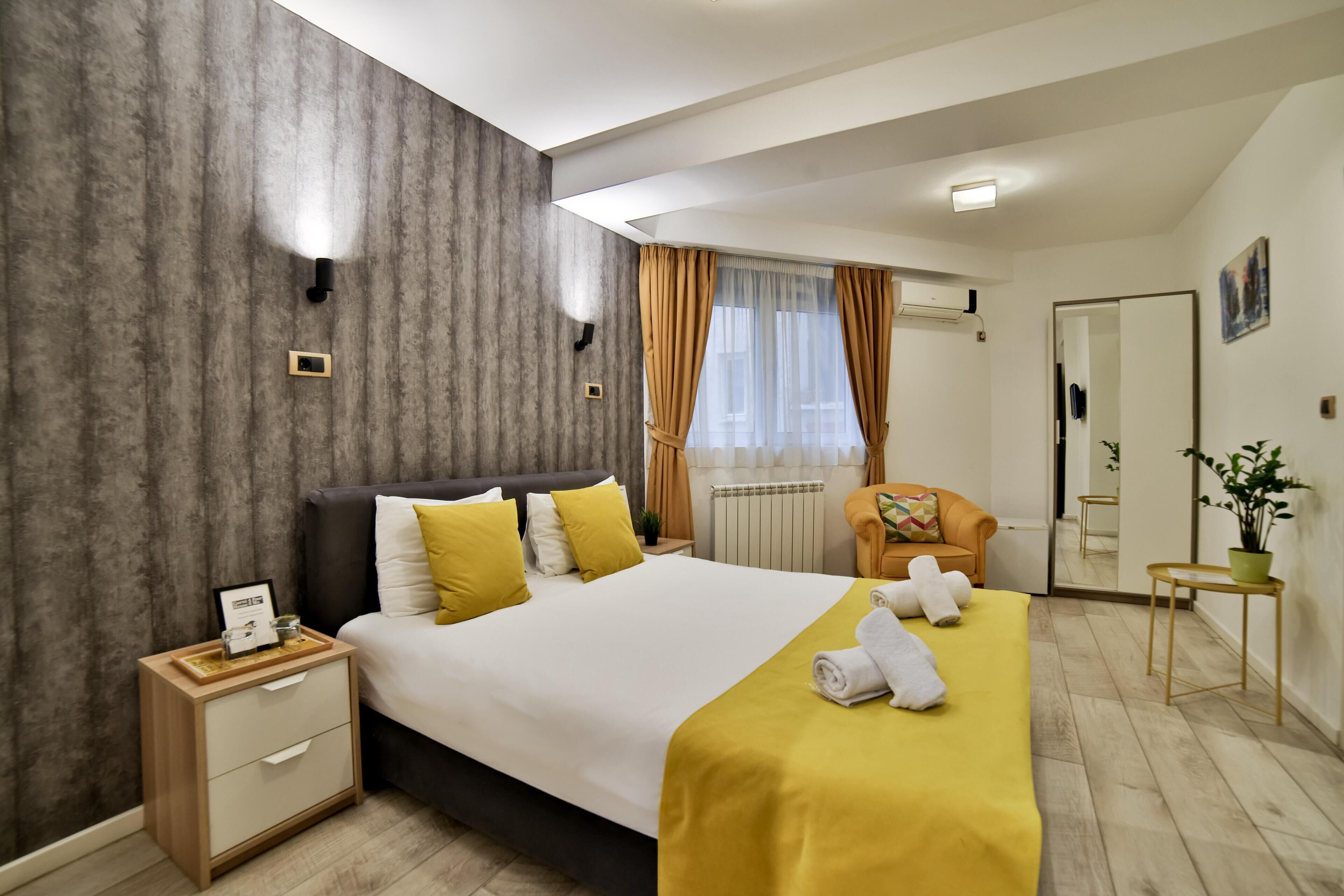 Habitación de hotel moderna con una cama grande, una mesita de noche, una silla, una planta en maceta y un espejo.