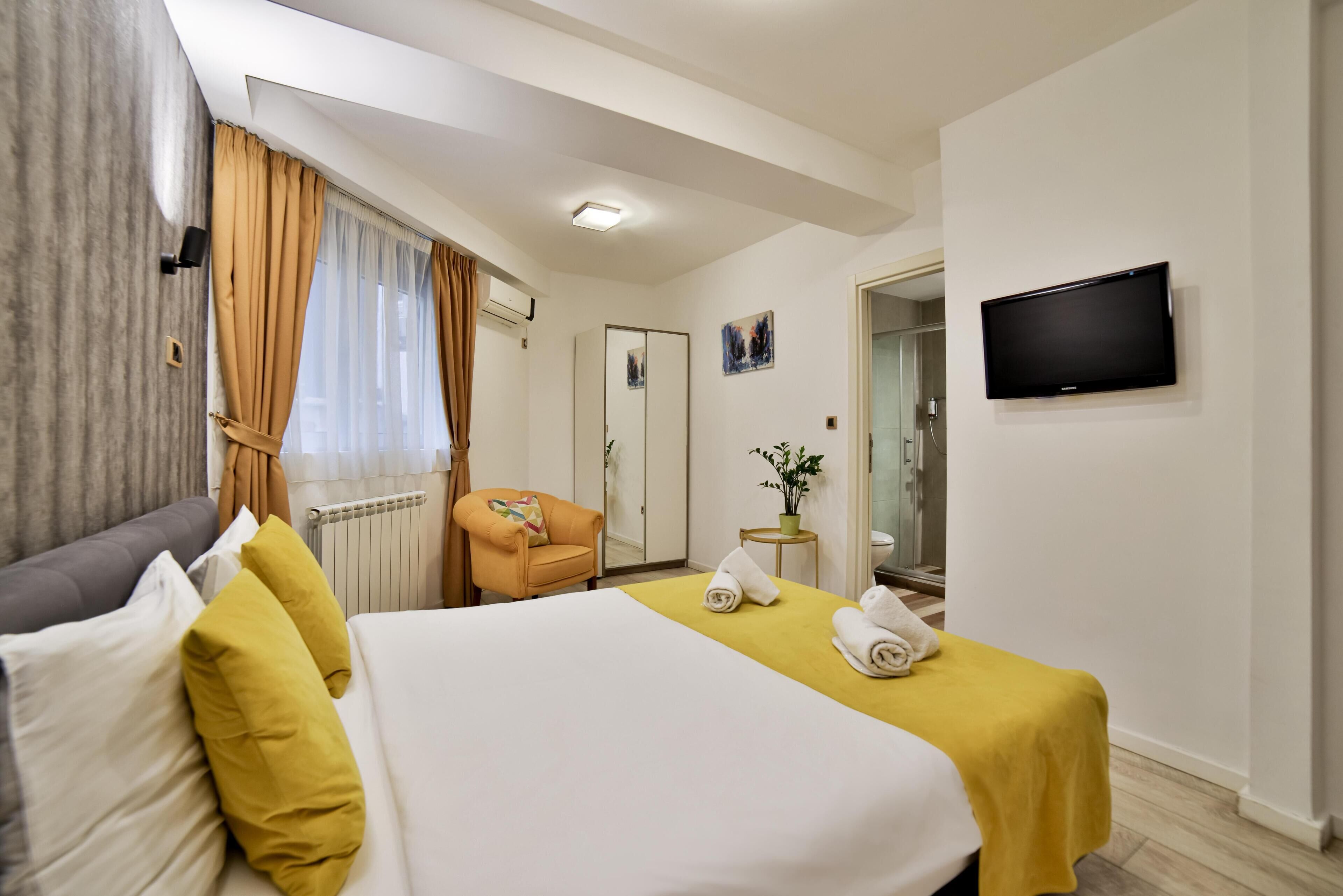 A hotel room with a bed, a chair, a TV, and a bathroom visible through an open door.