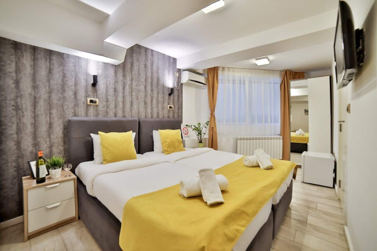 A modern hotel room with a large bed, a bedside table with a bottle and glasses, and a small plant.