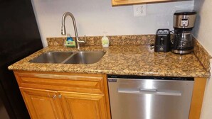 A kitchen with a granite countertop, stainless steel dishwasher, and a coffee maker.