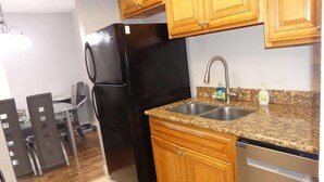 A kitchen with wooden cabinets, a granite countertop, a stainless steel sink, a black refrigerator, and a dishwasher.