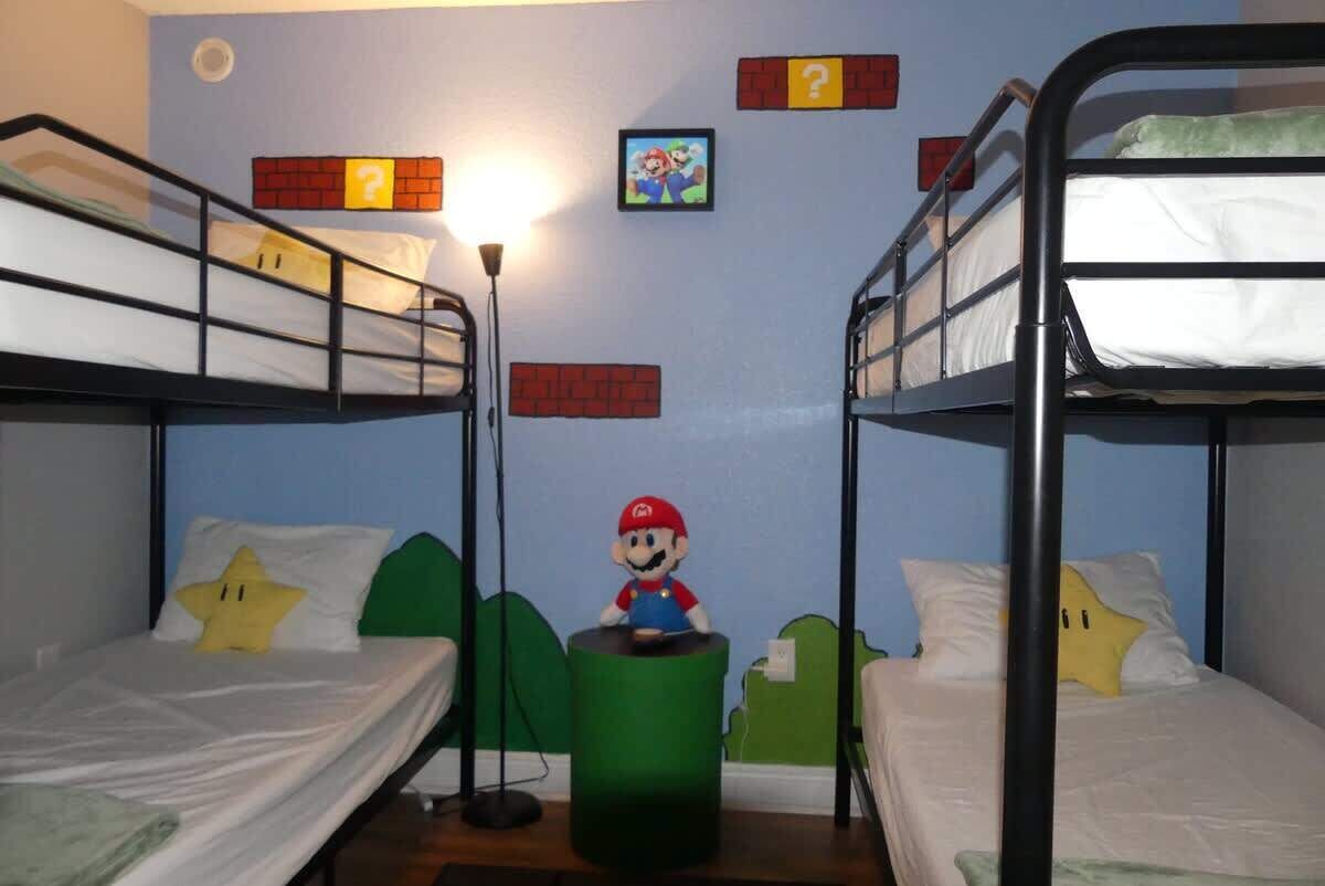 Une chambre avec des lits superposés, une figurine de Mario et des décorations murales sur le thème de Mario.
