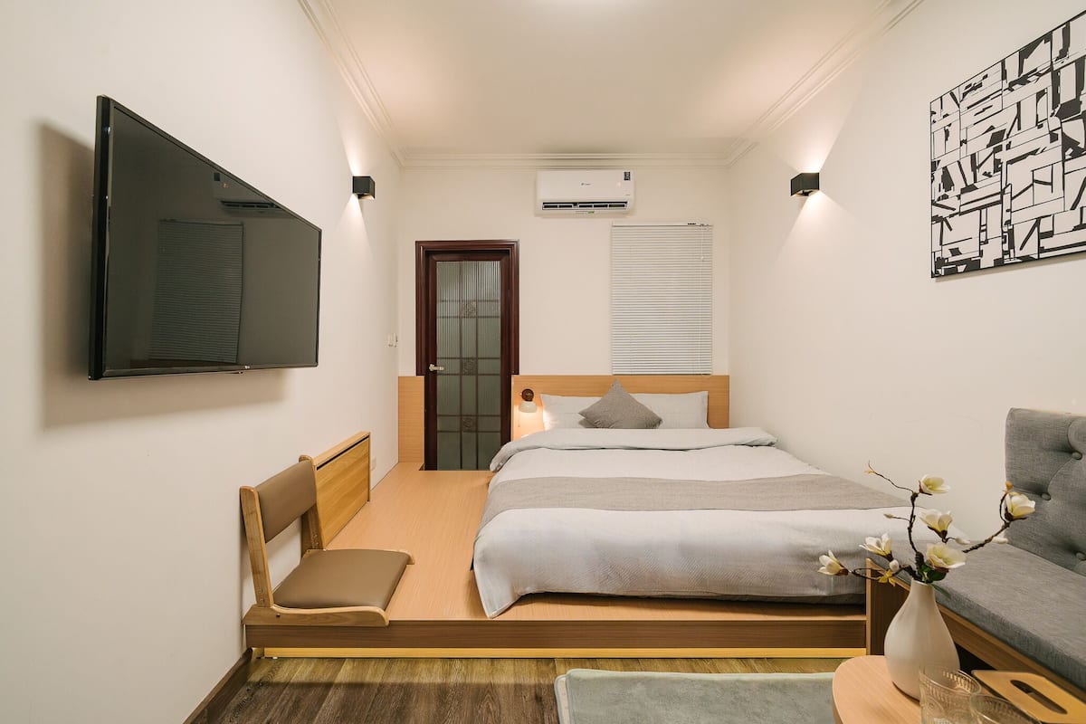 Un dormitorio moderno con cama, mesita de noche, silla y televisor de pantalla plana montado en la pared.