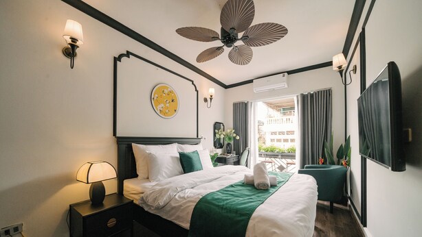 A hotel room with a bed, bedside lamp, ceiling fan, and a view of the outside balcony.