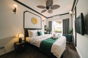 Habitación de hotel con cama, lámpara de noche, ventilador de techo y vista al balcón exterior.