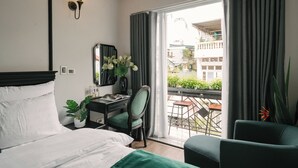 A hotel room with a bed, desk, chair, and a balcony with a view.