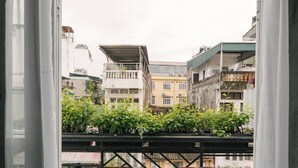 A balcony with two stools and a table, overlooking a cityscape with buildings and greenery.