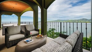 A balcony with wicker furniture, a round table, and a view of a lake and mountains. - Elegant 3BR Oceanview Condo with Pool, Gym & Shuttle to Flamingo Beach (Playa Flamingo)