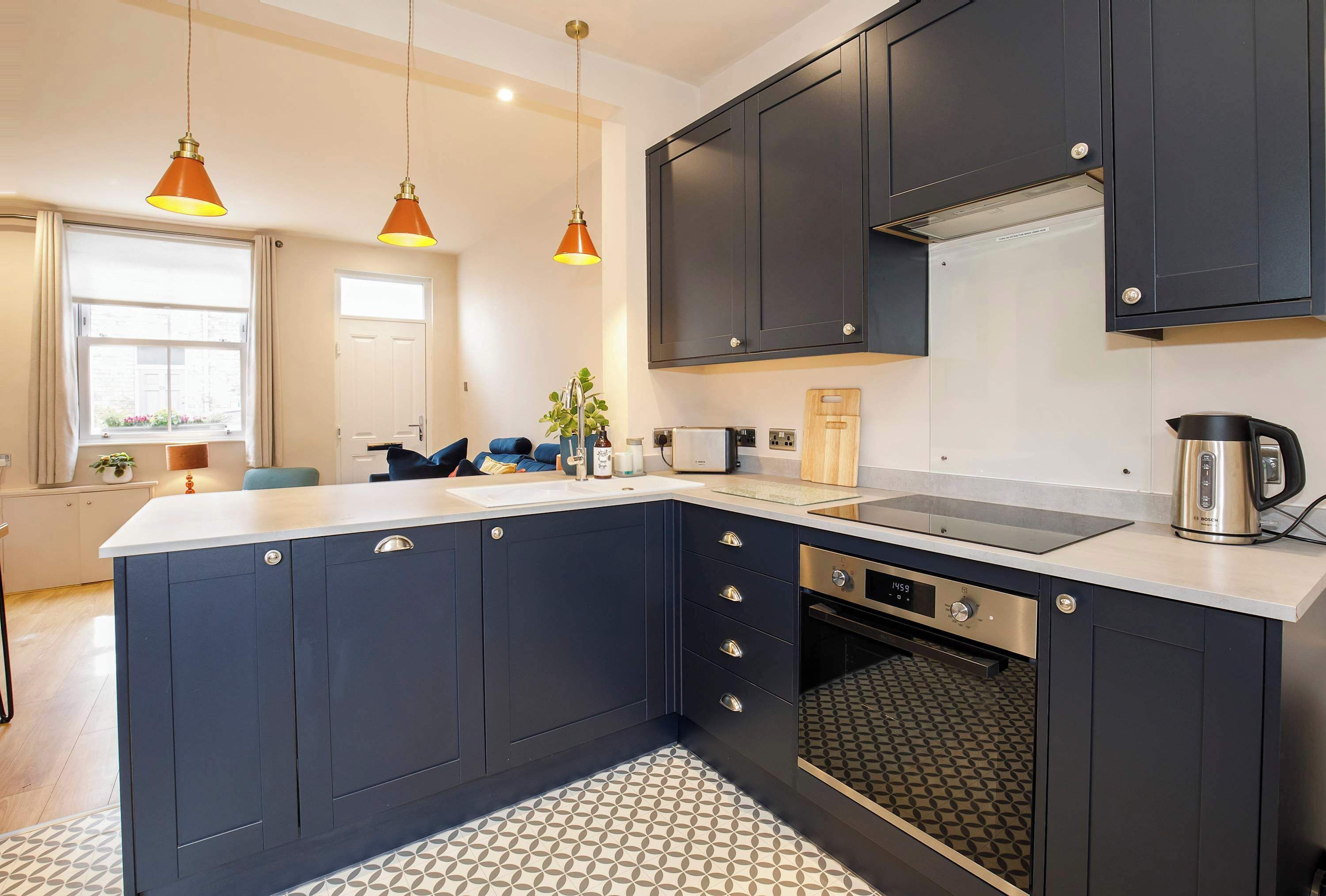 Une cuisine moderne avec des meubles de couleur sombre, un grand îlot central et des luminaires suspendus.