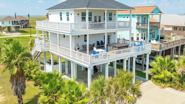 Una casa frente al mar de dos pisos, con balcón, mobiliario exterior y vista al océano.