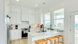 Una cocina moderna con armarios blancos, una isla central con taburetes, un amplio ventanal y vistas al exterior.