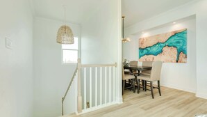 Comedor con mesa y sillas de madera, lámpara colgante y un cuadro en la pared.
