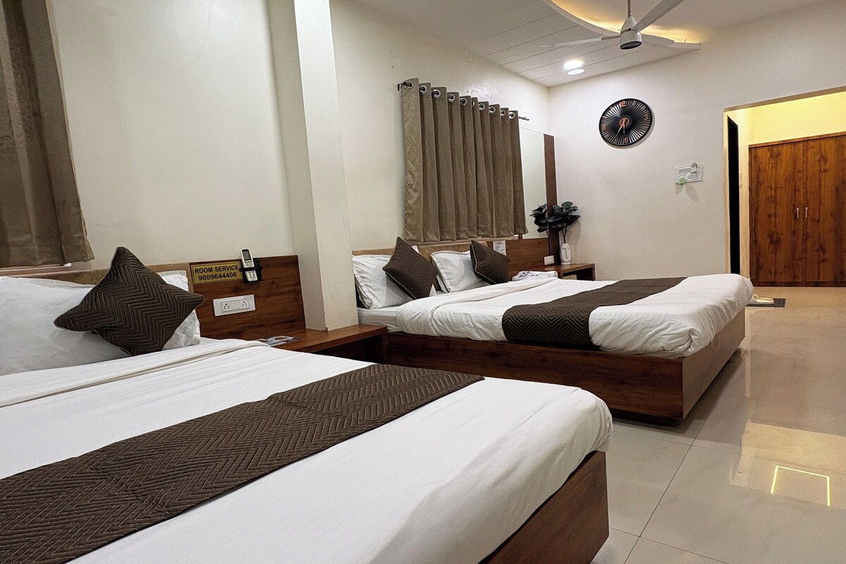 A hotel room with two beds, a bedside table with a phone, a clock on the wall, and a door leading to another room.