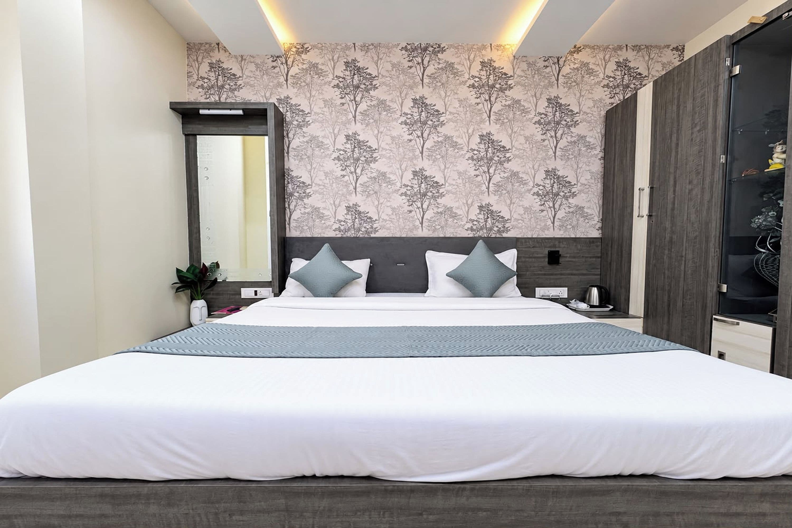 Una habitación de hotel moderna con una cama grande, un armario, un espejo y una pared con un diseño de árbol.