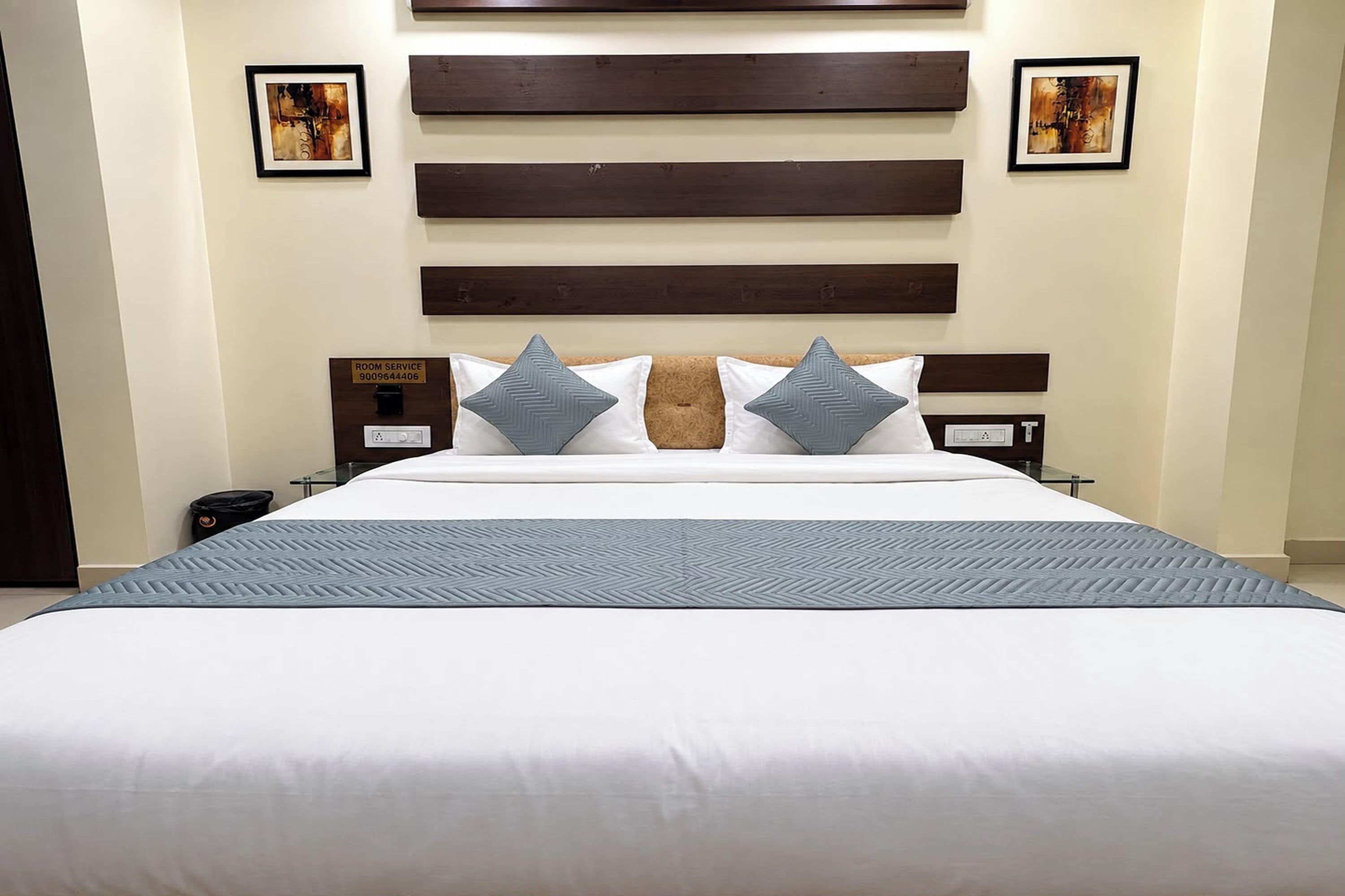 Une chambre d’hôtel avec un grand lit, deux tables de chevet, une tête de lit en bois et deux œuvres d’art encadrées accrochées au mur.