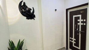 Un pasillo con suelo de baldosas, una planta en maceta, un adorno en la pared y una puerta con placa de número.