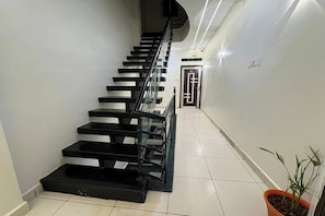 Un escalier avec des marches noires et des rampes en verre, menant à une porte ornée d’un motif géométrique.